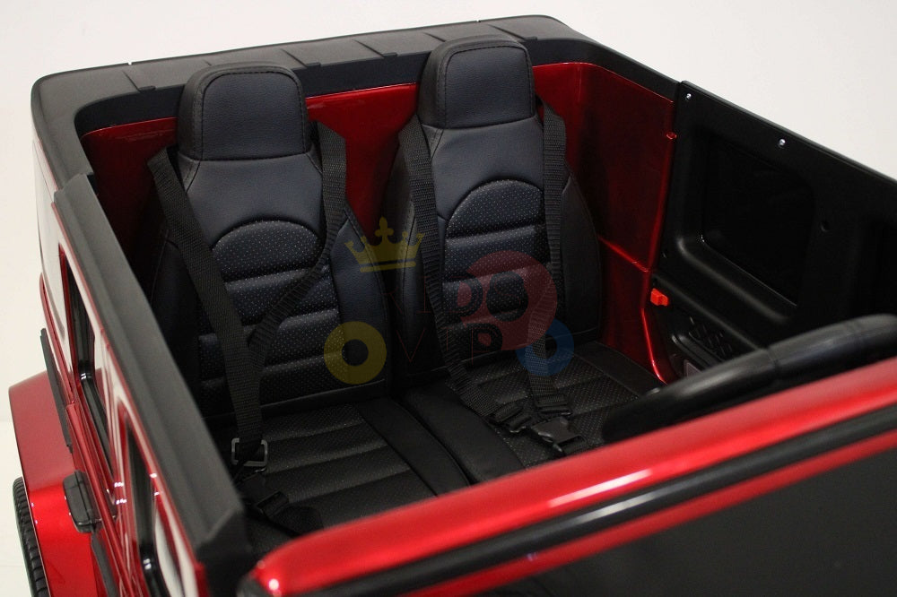 The 2 Seats 4x4 Official Mercedes Benz G63 Complete Edition Red 24V Kids Ride On Car with RC showcases a detailed interior, including two black seats with seatbelts. Designed for children, it emphasizes the back seat and features slightly ajar doors that reveal its intricate detailing.