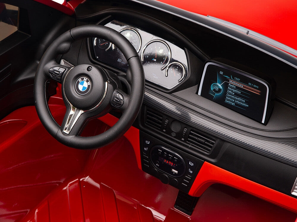 Interior of the Red 12V Licensed XXL BMW X6 Ride On Car features a logo-branded steering wheel, detailed gauges, a graphic screen, and a predominantly black and red realistic design operable via remote control.