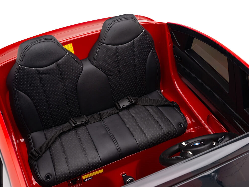 The Red 12V Licensed XXL BMW X6 Ride On Car features a realistic interior with two black seats complete with seatbelts, a detailed dashboard, and steering wheel.