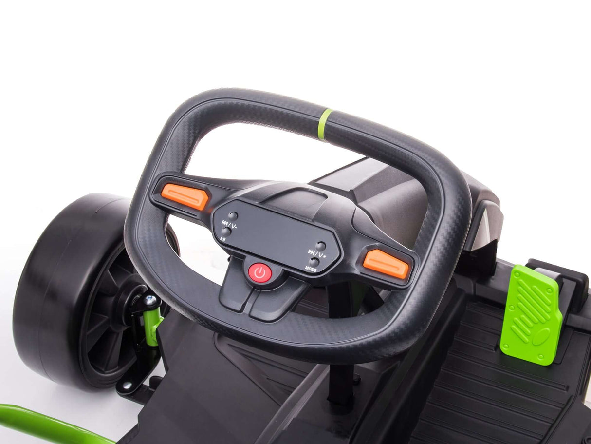 Close-up of a black steering wheel with orange buttons and green accents on the Big Kids Powerful 24V Speedster Drifting Go-Kart. The black dashboard shows a green pedal, with part of the rear wheel visible in the background.