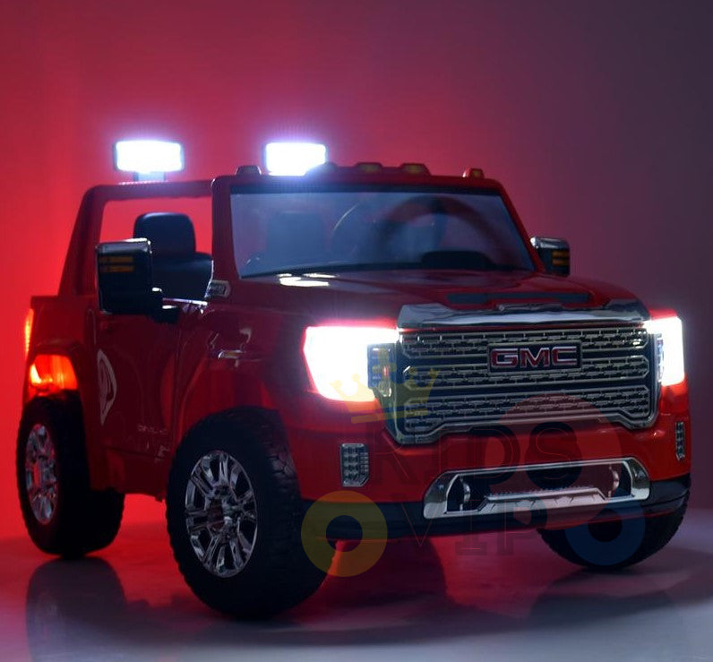The Black 2x12V Licensed 4WD GMC Sierra Kids Ride On Car lights up with bright front headlights and roof lights. It features shiny chrome details and large wheels, contrasting against a gradient red and dark background.