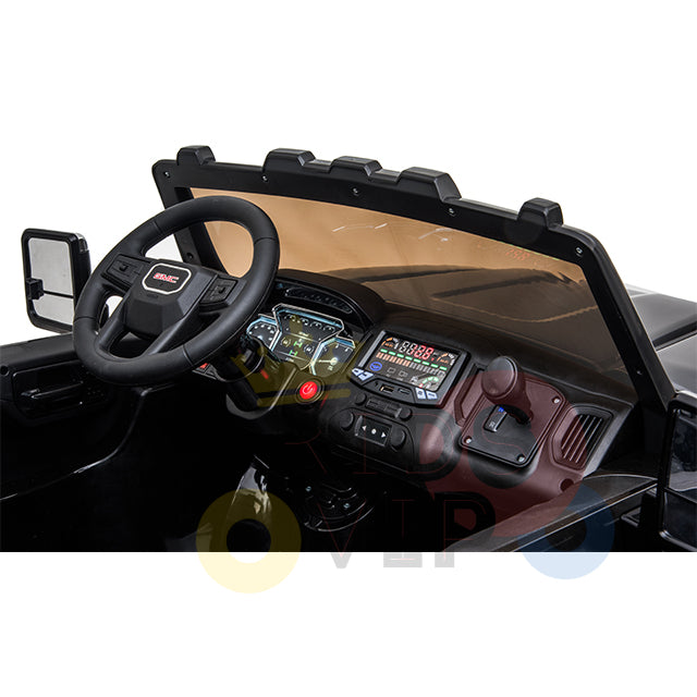 The dashboard of the Black 2x12V Licensed 4WD GMC Sierra Kids Ride On Car features a steering wheel with a centered logo, rearview mirror, and various controls. Its digital display has colorful buttons and gauges, mimicking a real GMC Sierra with detailed stickered features.