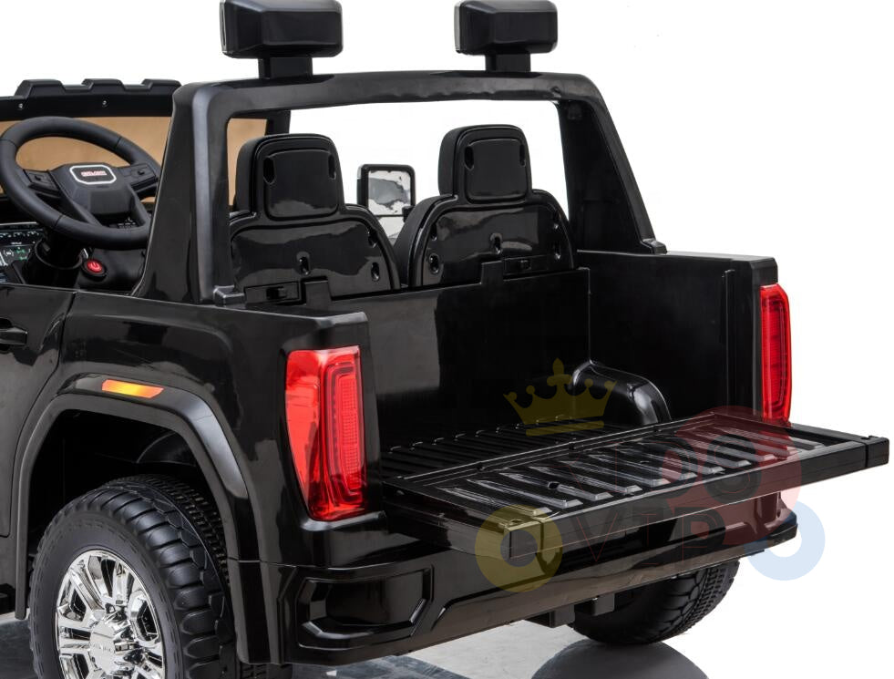 The Black 2x12V Licensed 4WD GMC Sierra Kids Ride On Car with RC features an open tailgate, two seats, a steering wheel, side mirrors, shiny wheels, red rear lights, visible dashboard controls, and parental remote control for added safety.
