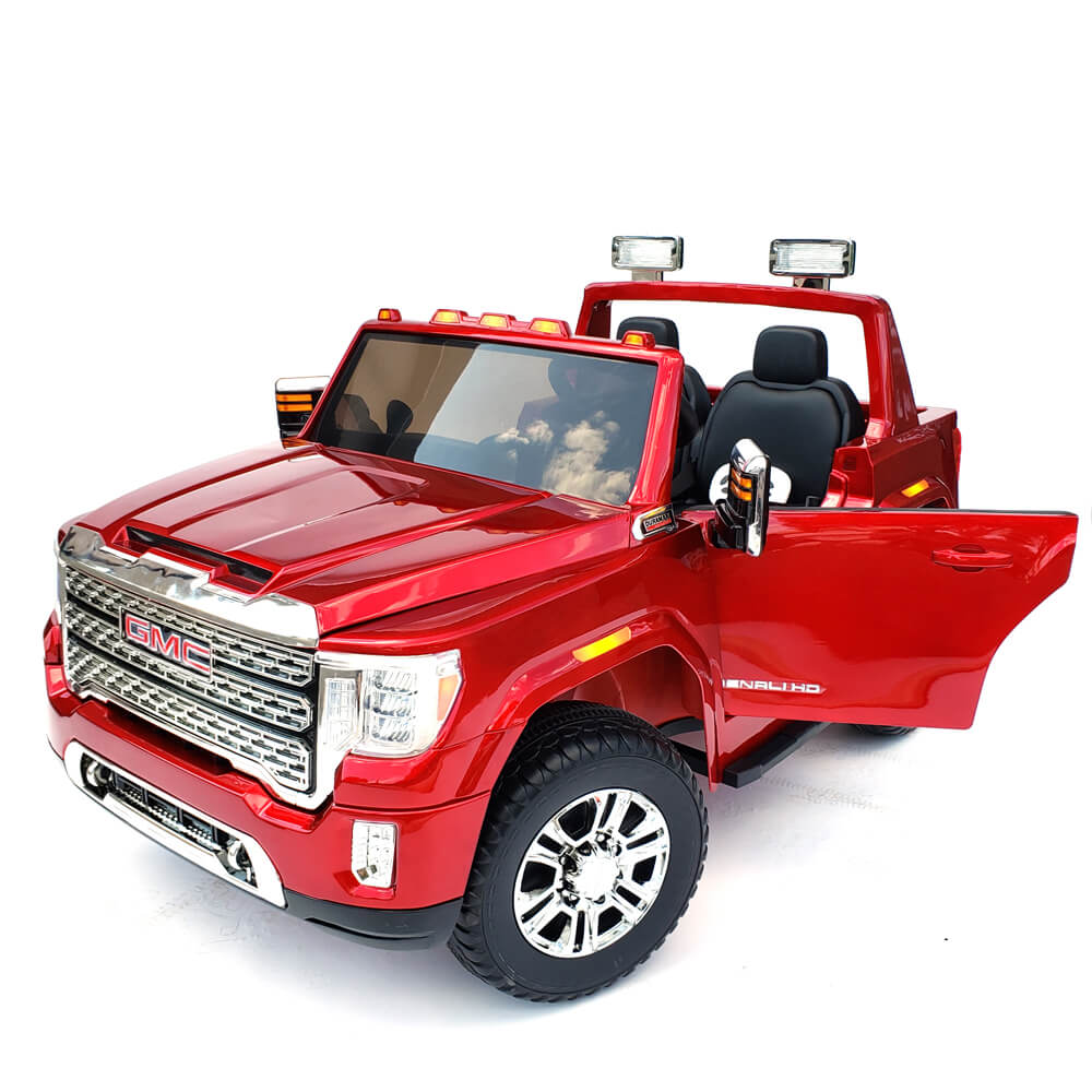 The High-Quality Passenger Side Door for the 12V/2 Seater GMC Sierra, a replacement part, enhances a red toy truck with shiny realism, including an open drivers door. Chrome accents and detailed grille make it stand out, while the beautifully reflective windshield captures sky and cloud reflections.