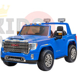 A blue 2-seater GMC Sierra 4WD kids ride-on car with chrome detailing, lights, detailed grille, large wheels, leather seats, and RC. The white background features a partial logo.