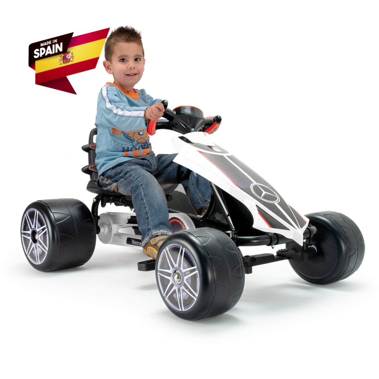 A young child in a blue sweater and jeans rides the INJUSA Officially Licensed Mercedes Pedal Go Kart for Kids with large wheels, featuring a logo and Made in Spain label, making it an ideal outdoor toy.