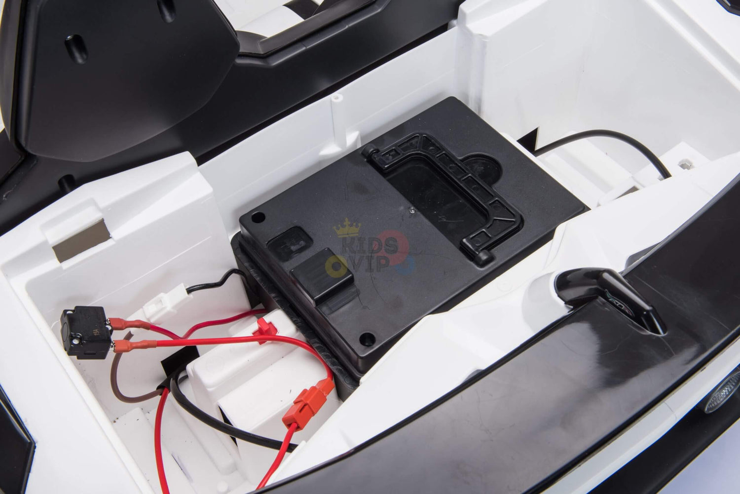 In the open compartment of the Upgrade Your Ride with the White 24v Lamborghini SVJ Drifting Kids Ride on Car, a 24V battery connects via red and black wires, housed in a sleek black casing within a white plastic interior, complete with drifting wheels for thrilling playtime.