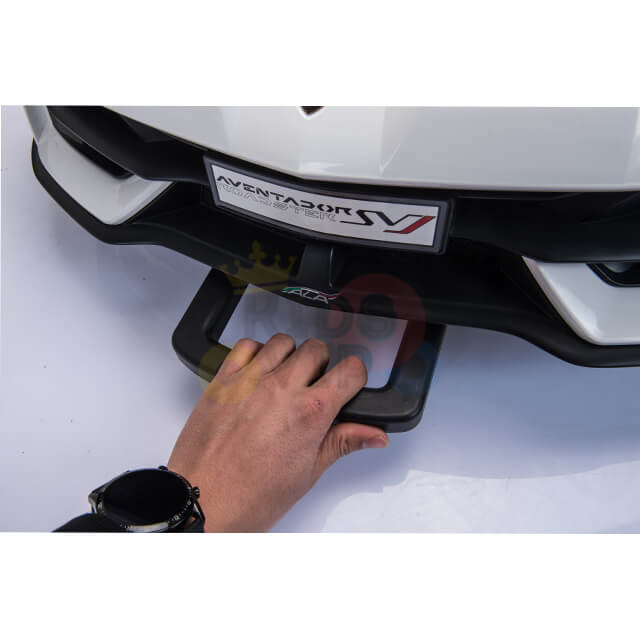 A hand with a black wristwatch tugs the tow hook on the sleek white cars front bumper, its license plate whispering Aventador SV and hinting at dreams of drifting wheels in the Upgrade Your Ride with the White 24v Lamborghini SVJ Drifting Kids Ride on Car.