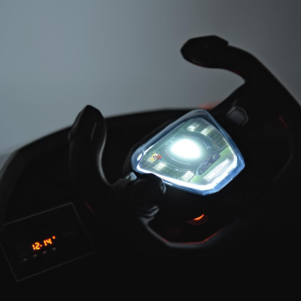 Close-up of the Green 12V Official Lamborghini Vision GT Kids Ride-On Car steering wheel, featuring a luminous display screen at the center. The bright screen partially lights up the dashboard, with a digital clock showing 12:14 in a dimly lit scene.
