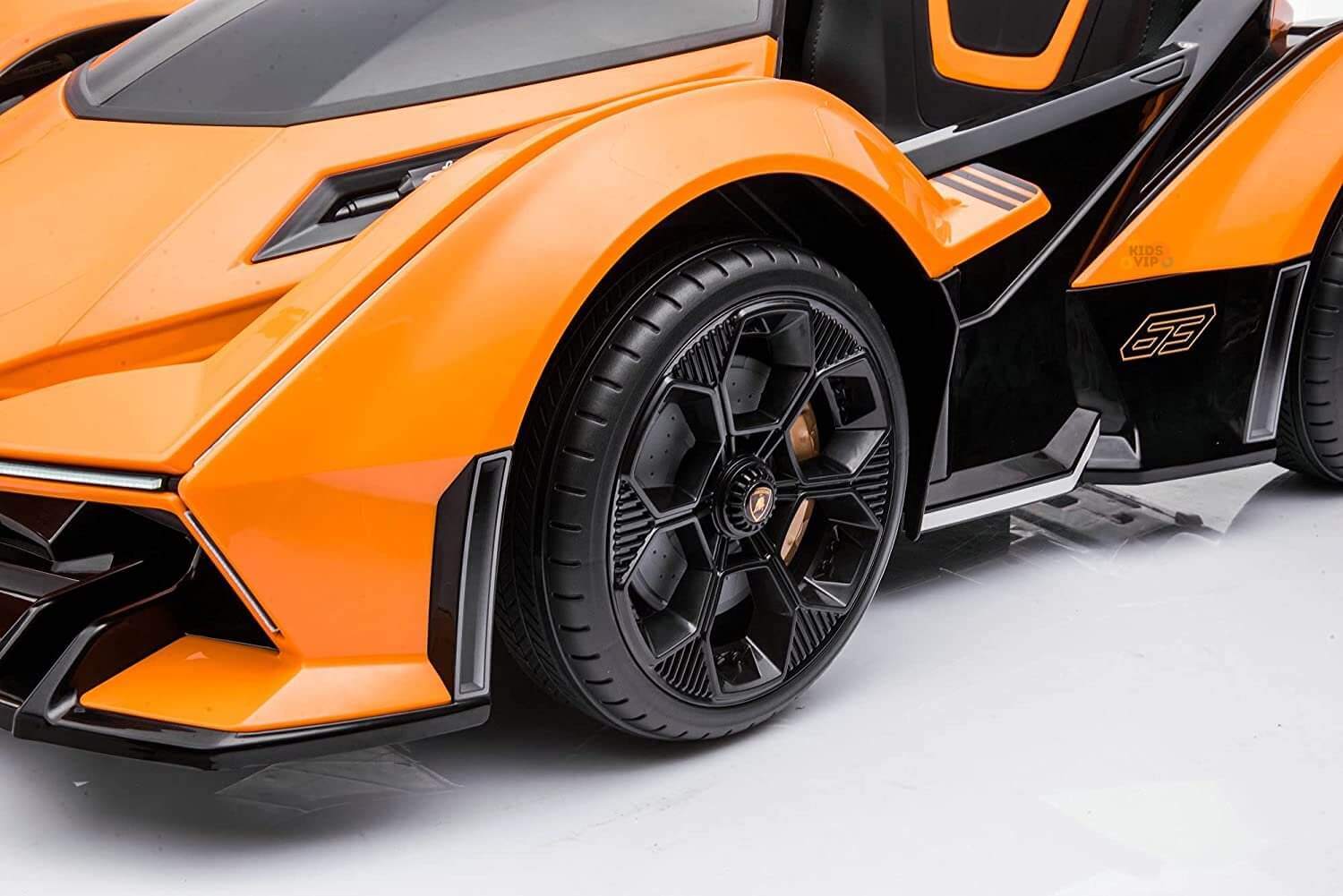 Close-up of the Orange 12V Official Lamborghini Vision GT Kids Ride-On car, emphasizing its sleek black and orange design. The image highlights the angular body, detailed black wheel rim, and sporty aesthetic.