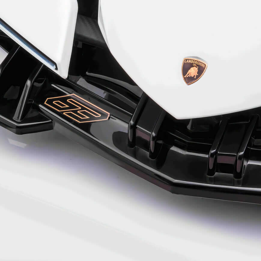 Close-up of a White 12V Official Lamborghini Vision GT Kids Ride on Cars front, highlighting the iconic gold Lamborghini emblem on the hood and a sleek black aerodynamic splitter with metallic accents.