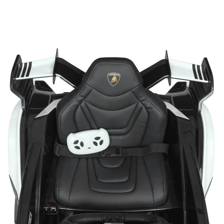 The White 12V Official Lamborghini Vision GT Kids Ride-on Car features an aerial view of a toy car seat, adorned with the Lamborghini logo. Its black, includes a white remote control, sports aerodynamic styling, a seatbelt for safety, and is powered by a 12V battery for thrilling rides.