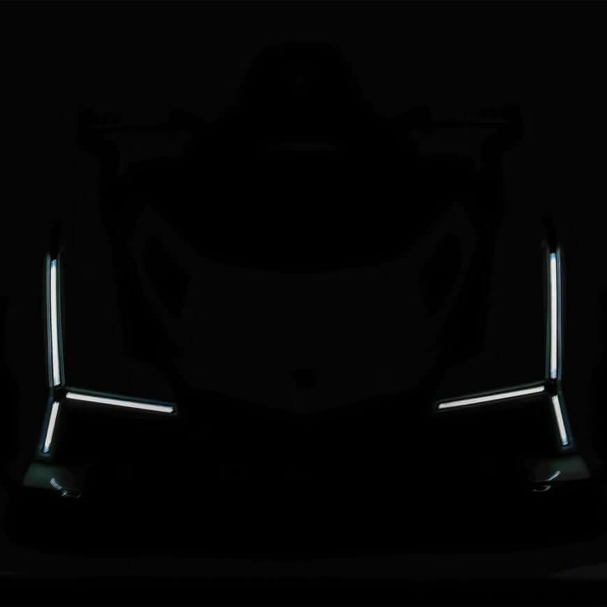 A dark image shows the silhouette of the White 12V Official Lamborghini Vision GT Kids Ride-On Car, its angular design highlighted by LED strips. The 12V battery-powered lights form vertical lines on each side, suggesting the front view of this futuristic marvel.