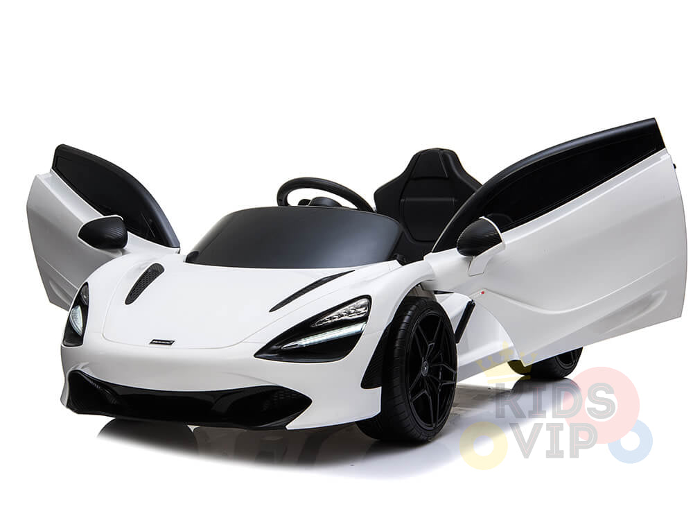 A white 12V McLaren 720S Kids Licensed Ride On Car, complete with scissor doors, sleek black accents, an upgraded steering wheel, and rubber wheels, is displayed on a smooth reflective surface.