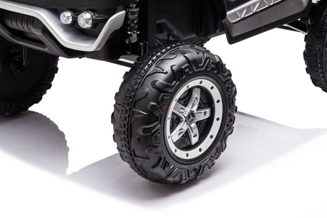 Close-up of a rugged off-road tire and suspension system reminiscent of the Black Official 12V Mercedes Unimog Junior 4X4 Kids Ride On UTV. The deep tread is ideal for tough terrains, perfectly complementing the kids car on a smooth white surface.