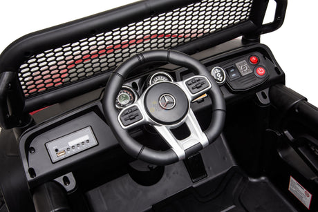 Close-up of the interior in the White 12V/4X4 Official Mercedes Unimog Junior Ride On UTV, showing a steering wheel with a logo, gear shift, buttons, mesh grille, speedometer, and controls—all in black with red accents.