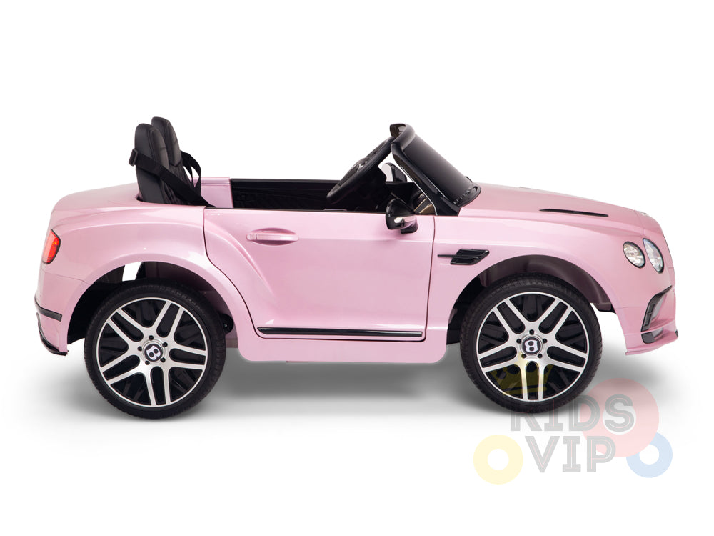 The Pink 12V Bentley GTC Kids Licensed Ride On Car boasts a sleek design with black seats, a detailed dashboard, and shiny silver wheels. It is branded with the KIDS VIP logo and comes equipped with a parental remote for modern play.