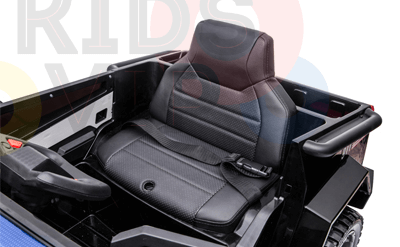 Inside the cabin of the Futuristic 12V Police Truck Ride On for Kids and Toddlers, a black leather seat with stitching detail and a seatbelt is visible. The steering wheel appears partially on the left, set against faint colorful text in the background.