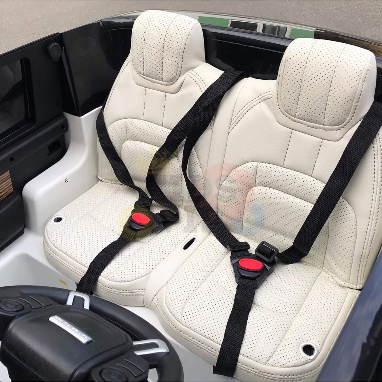 The 24V Complete White on White Edition Range Rover Kids Ride On Car includes two white perforated leather seats with black seatbelts, a small black steering wheel, part of the dashboard visible, and a sandy-colored floor mat.