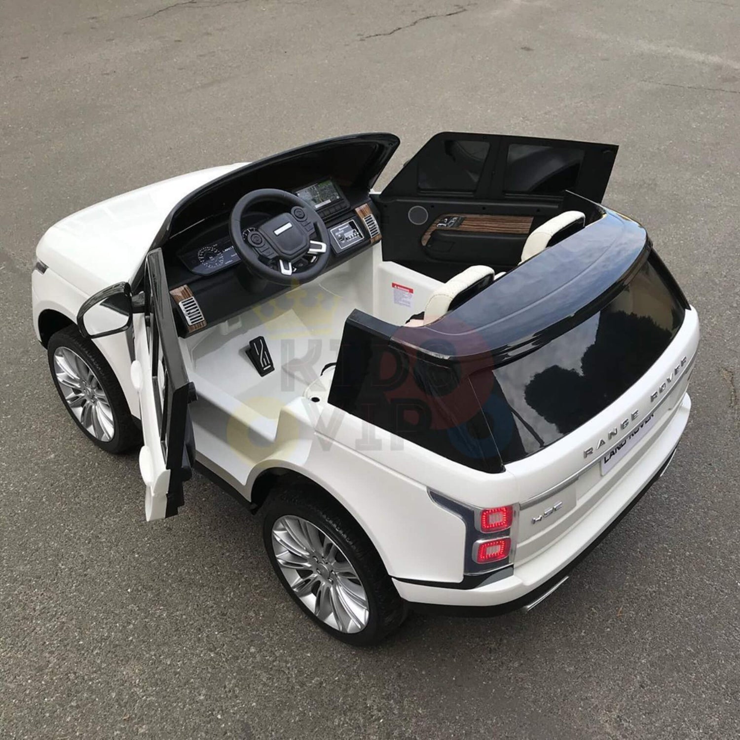 A white 24V Range Rover Kids Ride On Car with RC and MP4 stands on the gray pavement, its doors open to reveal a detailed interior with steering wheel and dashboard, bringing realism and excitement to young adventurers.