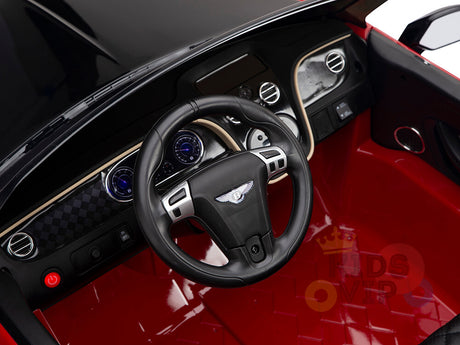 Close-up of a black and red cockpit from the Red 12V Bentley GTC Kids Licensed Ride On Car, featuring a detailed steering wheel with logo, dashboard dials, and modern control buttons.