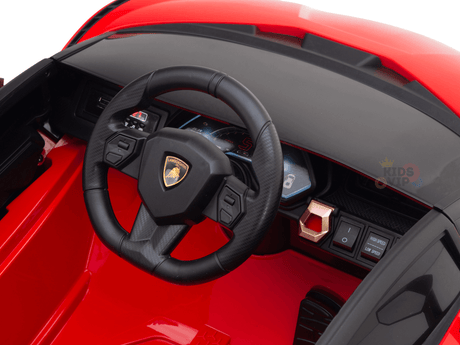 Detailed interior view of the Red Official 12V Sport Edition Lamborghini Sian Kids and Toddlers Ride On Car, showcasing a black steering wheel with logo, digital dashboard, control buttons, and realistic butterfly doors that emulate a luxury sports car.