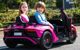 Two children sit smiling in a small, pink toy car on a sunny day. The car is a Pink 24V/180W Lamborghini SV Limited XXL Edition, reaching up to 10MPH, parked on a paved surface with greenery in the background.