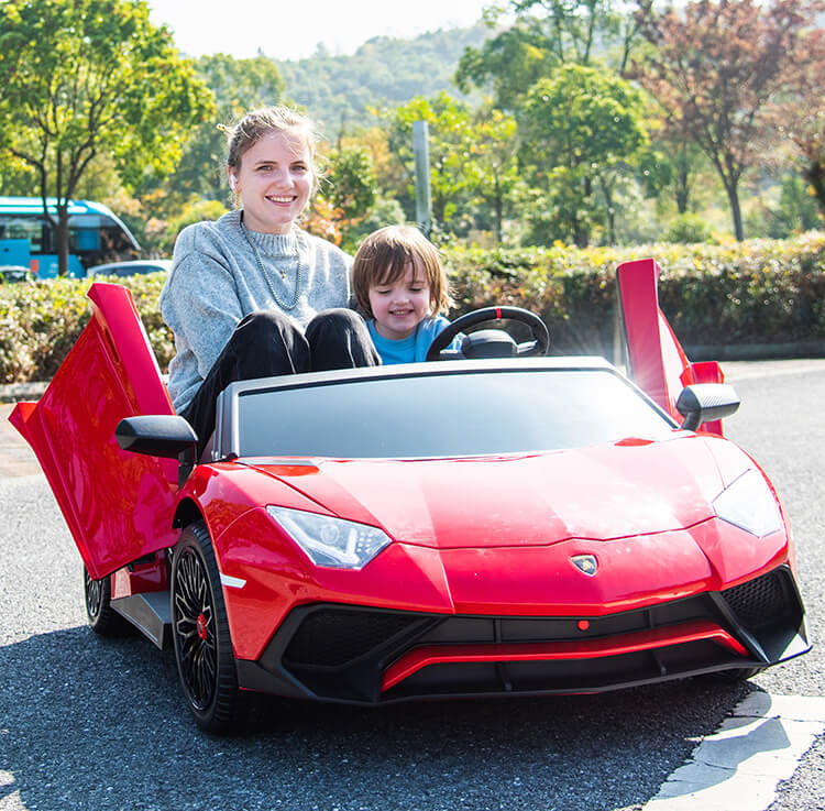 A woman and child enjoy a sunny day in a red Giant Official Limited Edition Lamborghini SV 24V/180W for Big Kids, with open scissor doors. Trees and a bus are visible in the background as they smile in this joyful scene.